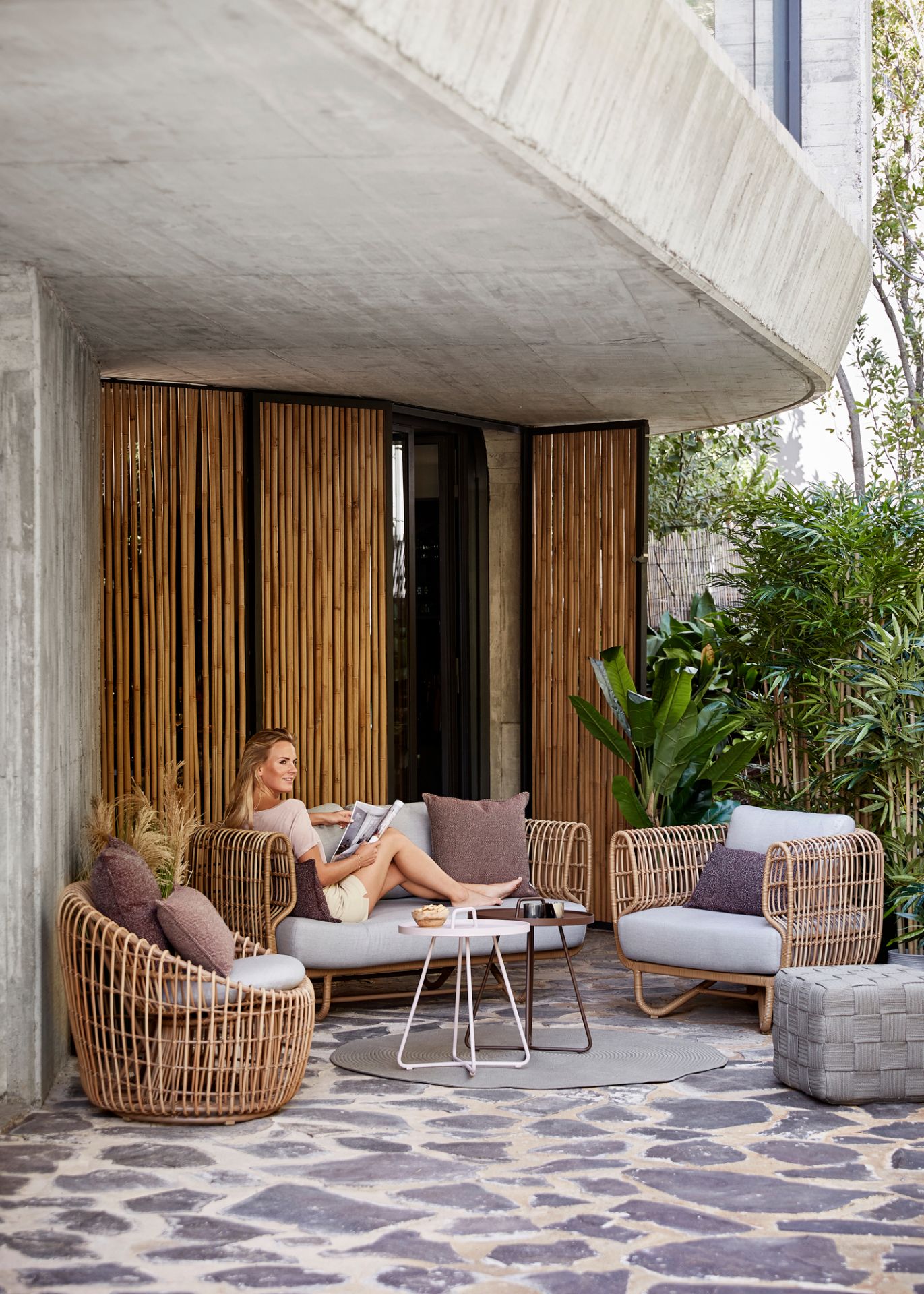Frau entspannt auf Cane-Line Nest Outdoor Sofa mit Rattan-Sessel und Beistelltisch.