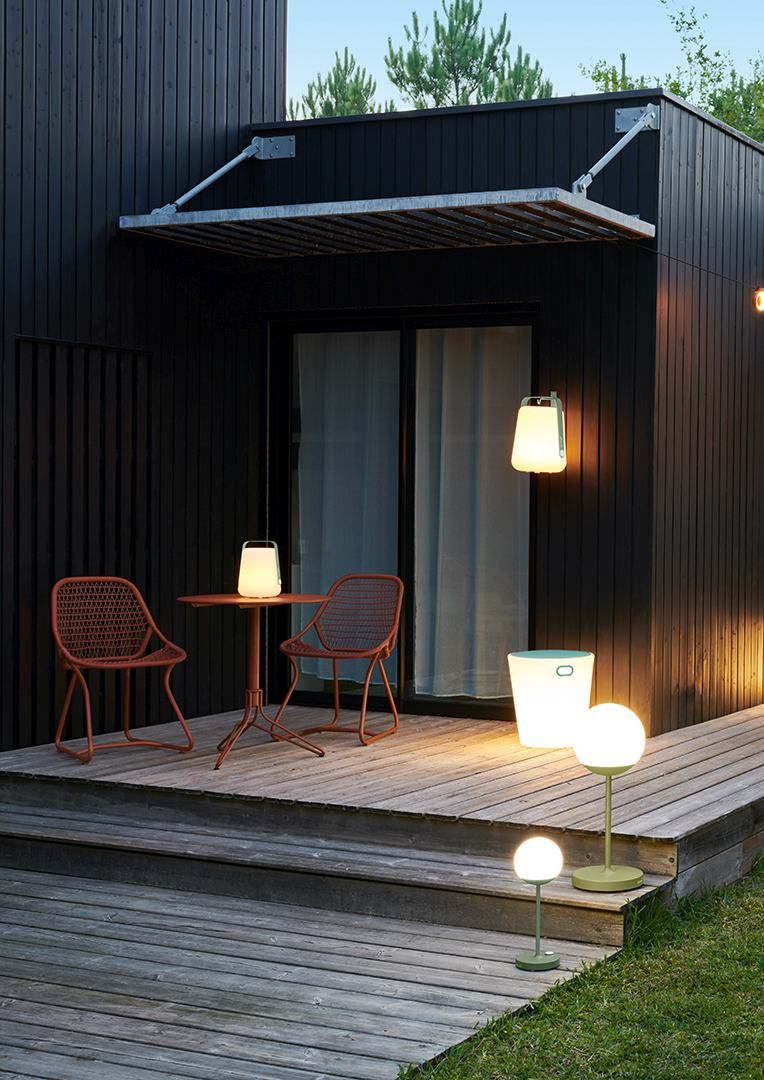 Zwei rote Sixties Outdoor Stühle von Fermob mit Tisch und Gartenbeleuchtung auf einer Holzterrasse.