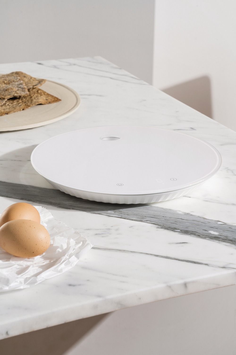 Weiße Alessi Plissé Digitale Küchenwaage auf Marmor, neben Eiern und Crackern.