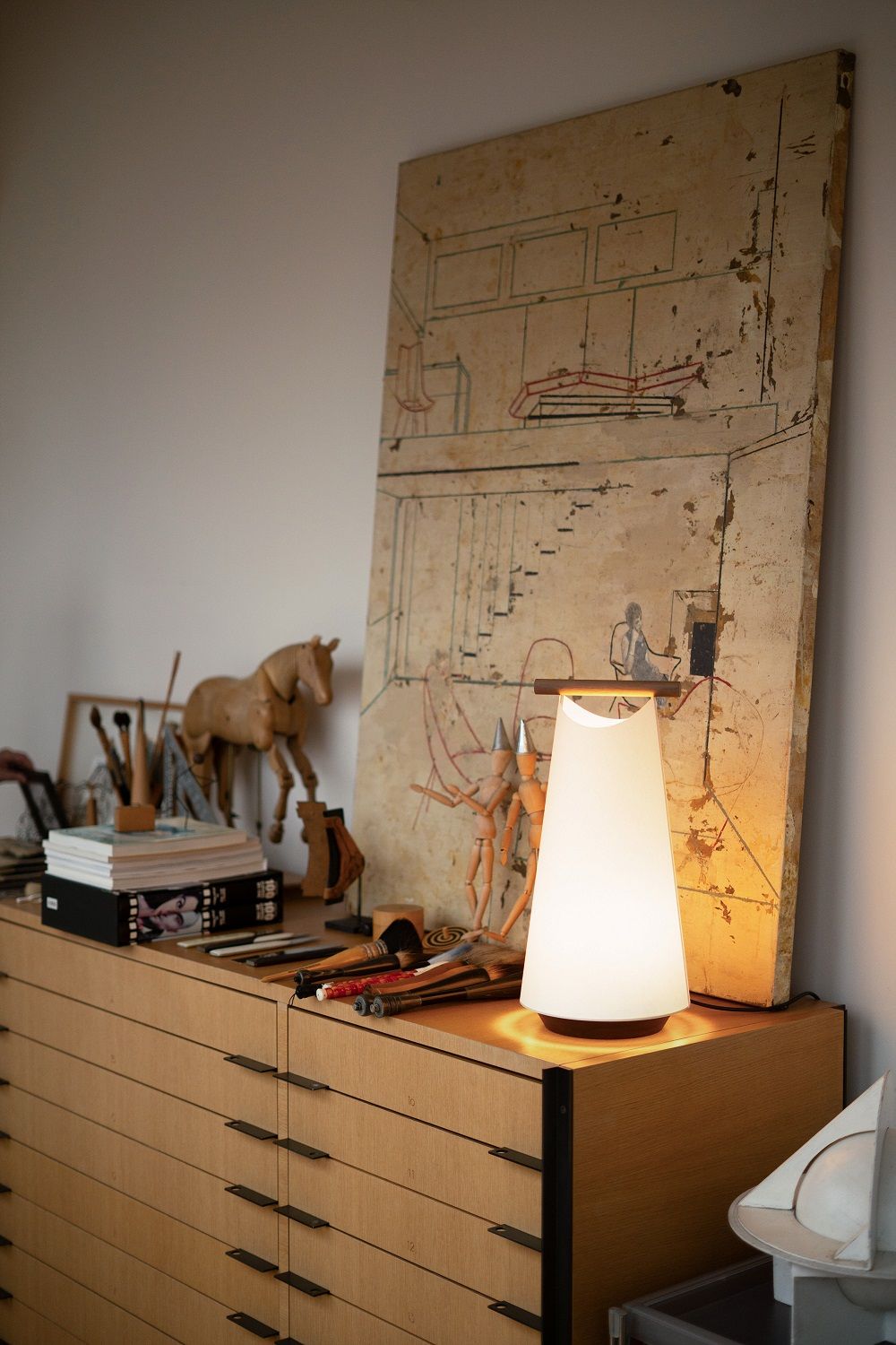 Nomon Catay Tischleuchte: Moderne Akku-Tischlampe aus Opalglas auf einer Holzkommode mit Kunstobjekten.