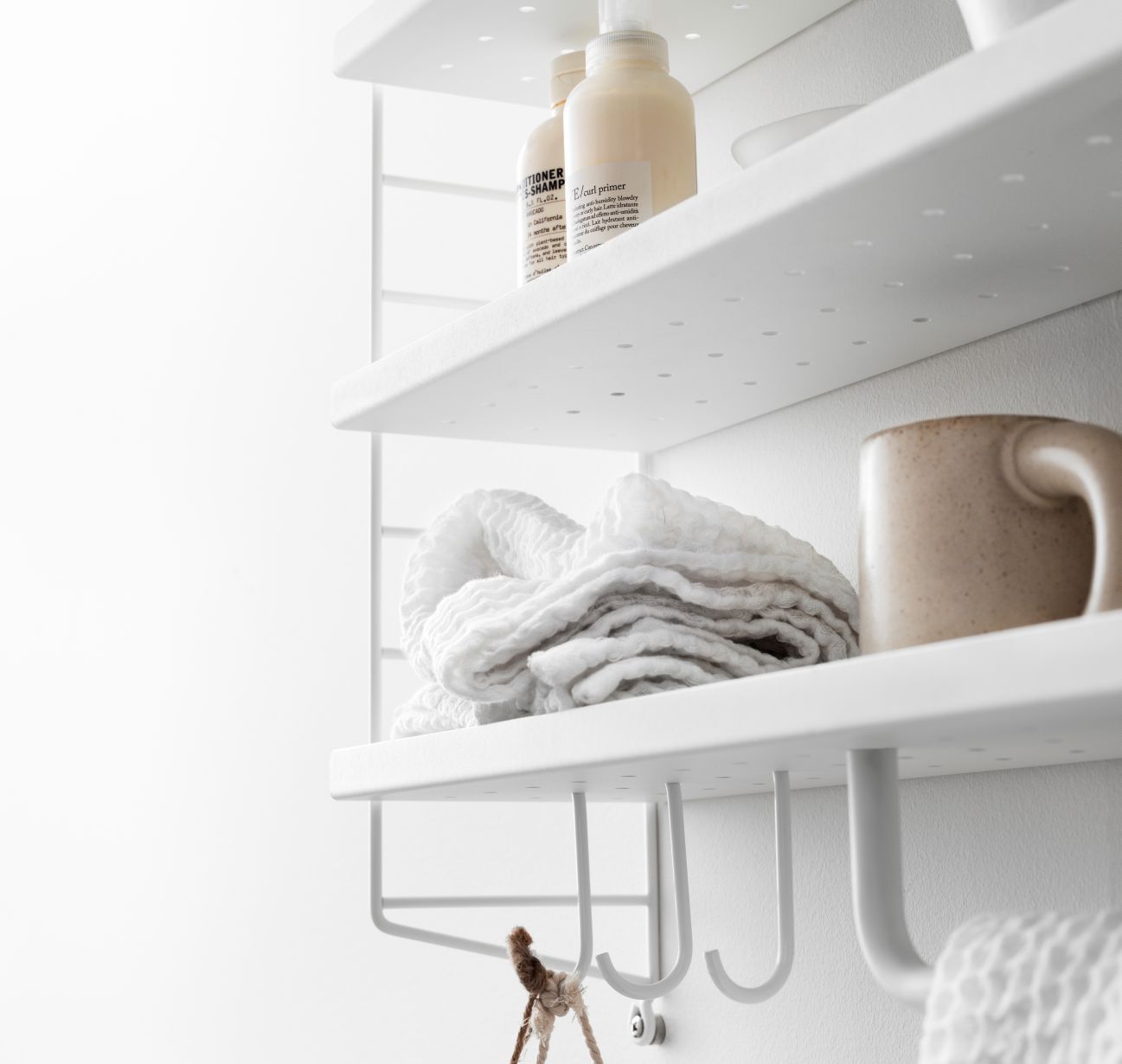 Detailaufnahme eines weißen String Furniture Regals (B 58 cm) mit Handtuch, Tasse und Pflegeprodukten.