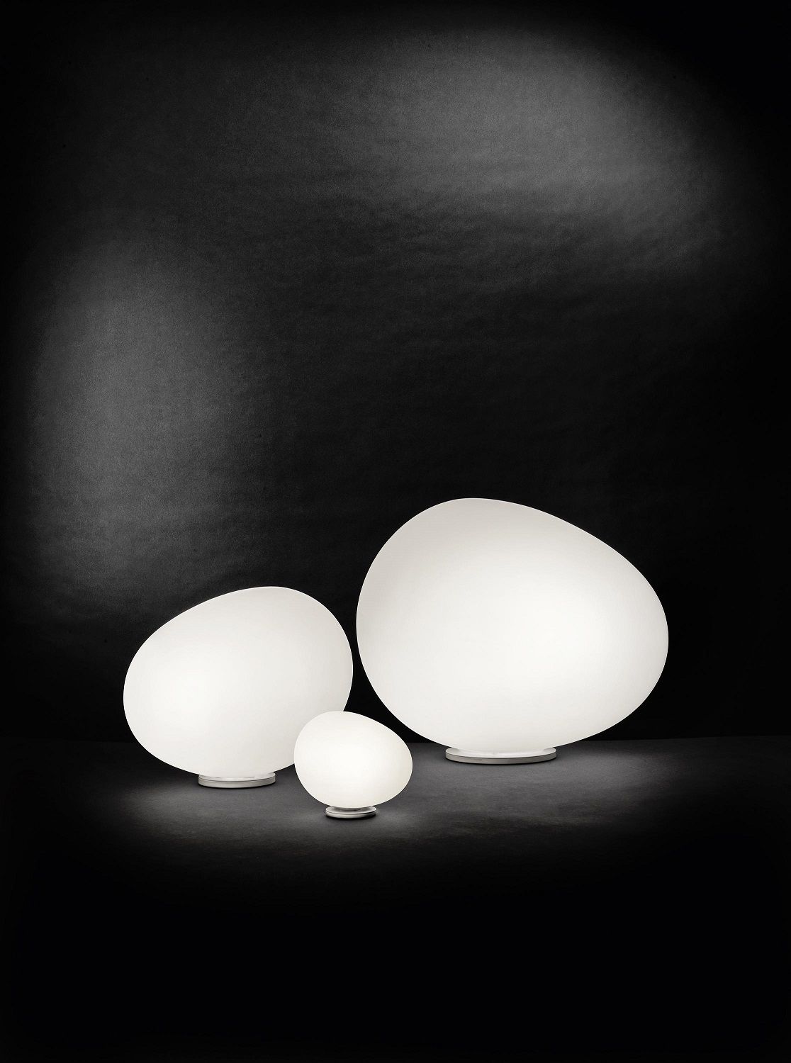 Drei weiße Gregg Tischleuchten von Foscarini in verschiedenen Größen vor schwarzem Hintergrund.