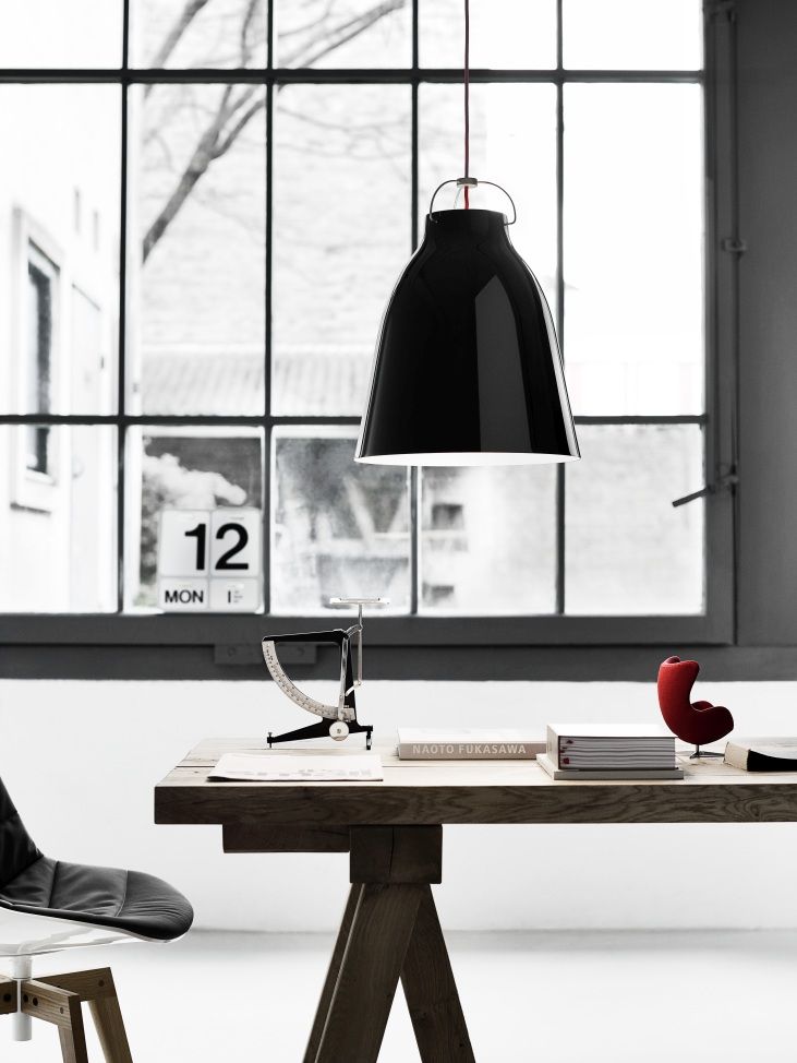 Schwarze Caravaggio Pendelleuchte von Fritz Hansen über einem Holztisch mit Büchern und Dekoration vor Fenster.
