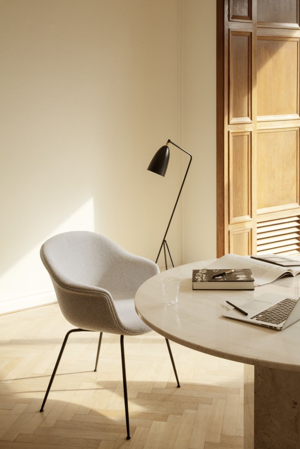 Runder Esstisch aus Travertin, möglicherweise ein Gubi Epic Tisch, mit Stuhl, Lampe und Laptop.