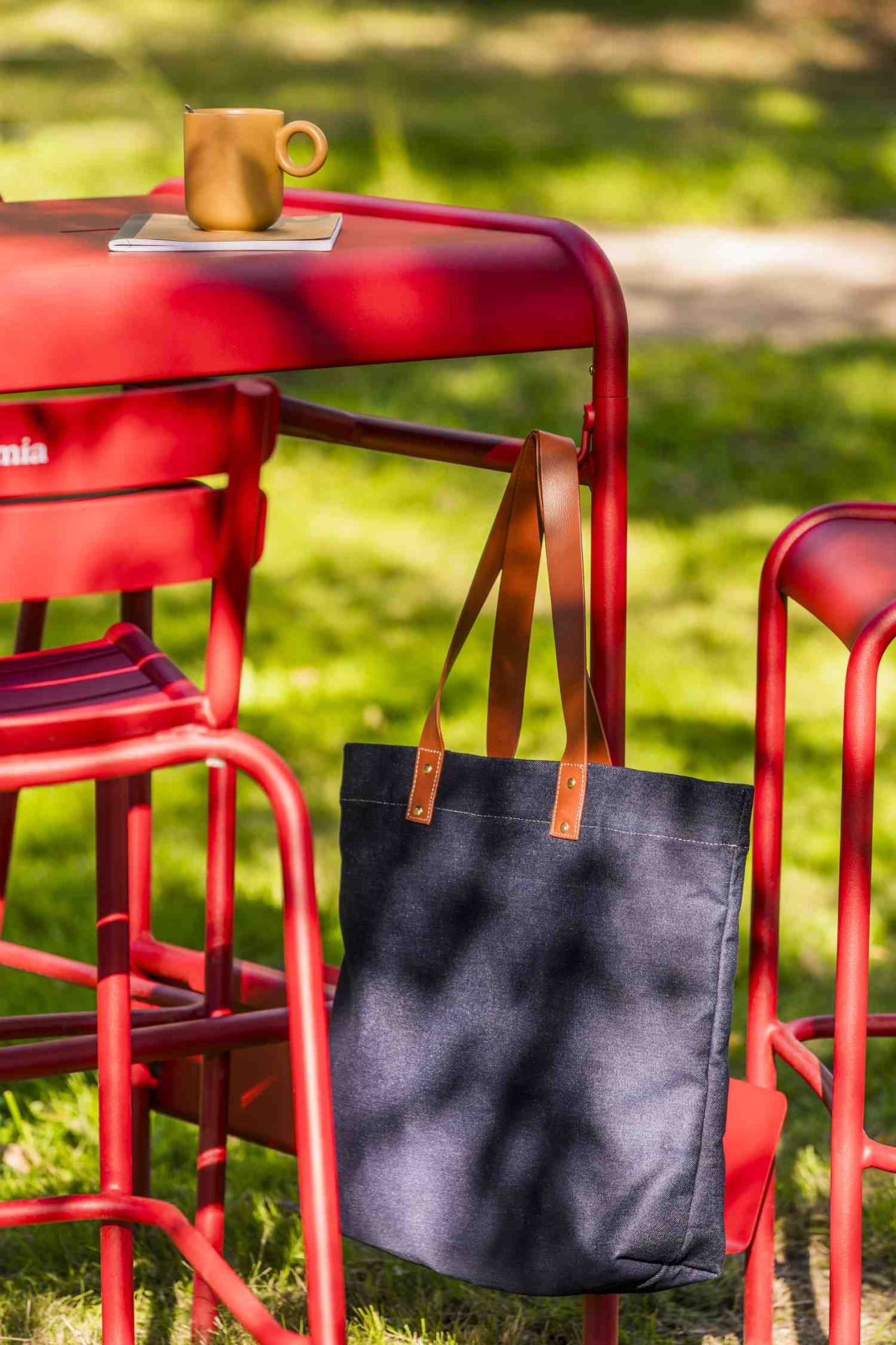 Roter Luxembourg Stehtisch im Freien mit Tasse, Notizbuch und Tasche. Outdoor-Möbel für Garten und Terrasse.