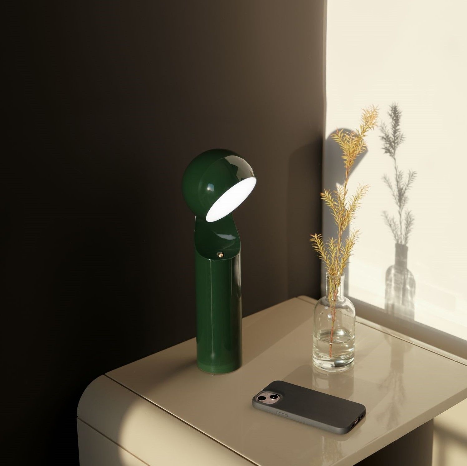 Grüne Mono Portable Akkuleuchte/Tischleuchte auf Nachttisch mit Vase und Handy.