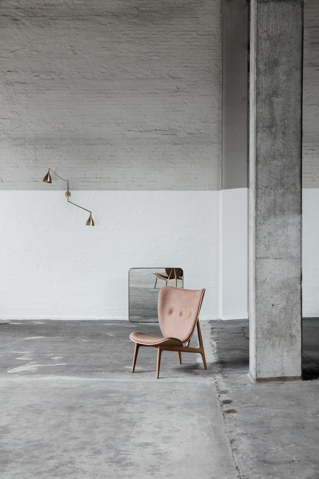NORR11 Elephant Lounge Chair Sessel in hellem Leder und Holzgestell vor Spiegel und Betonpfeiler.