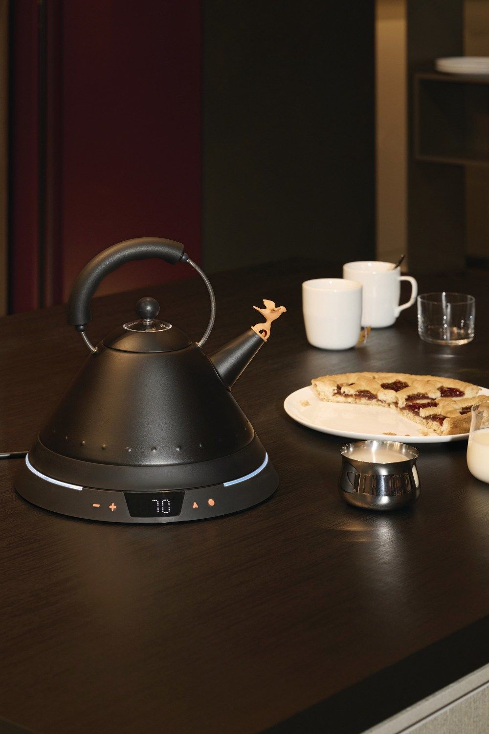 Schwarzer Alessi Wasserkocher MG32TC mit Temperaturregelung, Vogelfigur am Ausguss, Tasse, Kuchen und Milch.