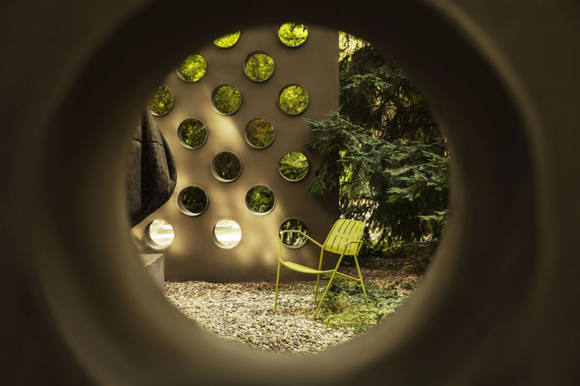 Gelber Osmo Outdoor Stuhl von Prostoria im Garten, gesehen durch eine kreisförmige Öffnung.