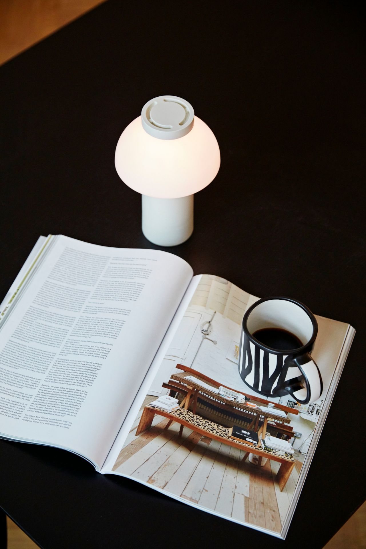 Cremefarbene Hay PC Portable Akkuleuchte auf Tisch neben Magazin und Kaffeetasse. Moderne Tischlampe für gemütliches Licht.