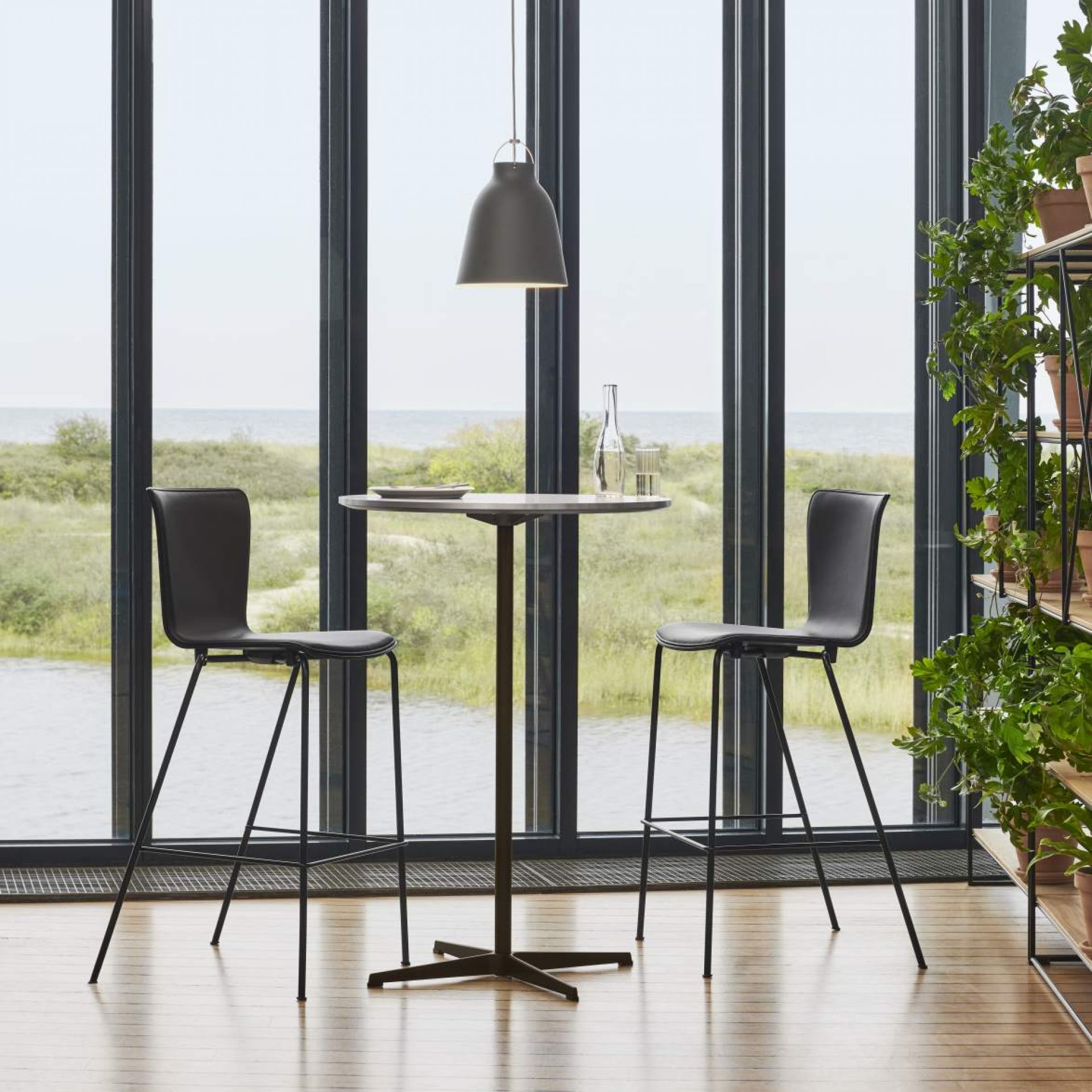 Zirkular Stehtisch von Fritz Hansen mit zwei Barhockern vor einem Fenster mit Meerblick.