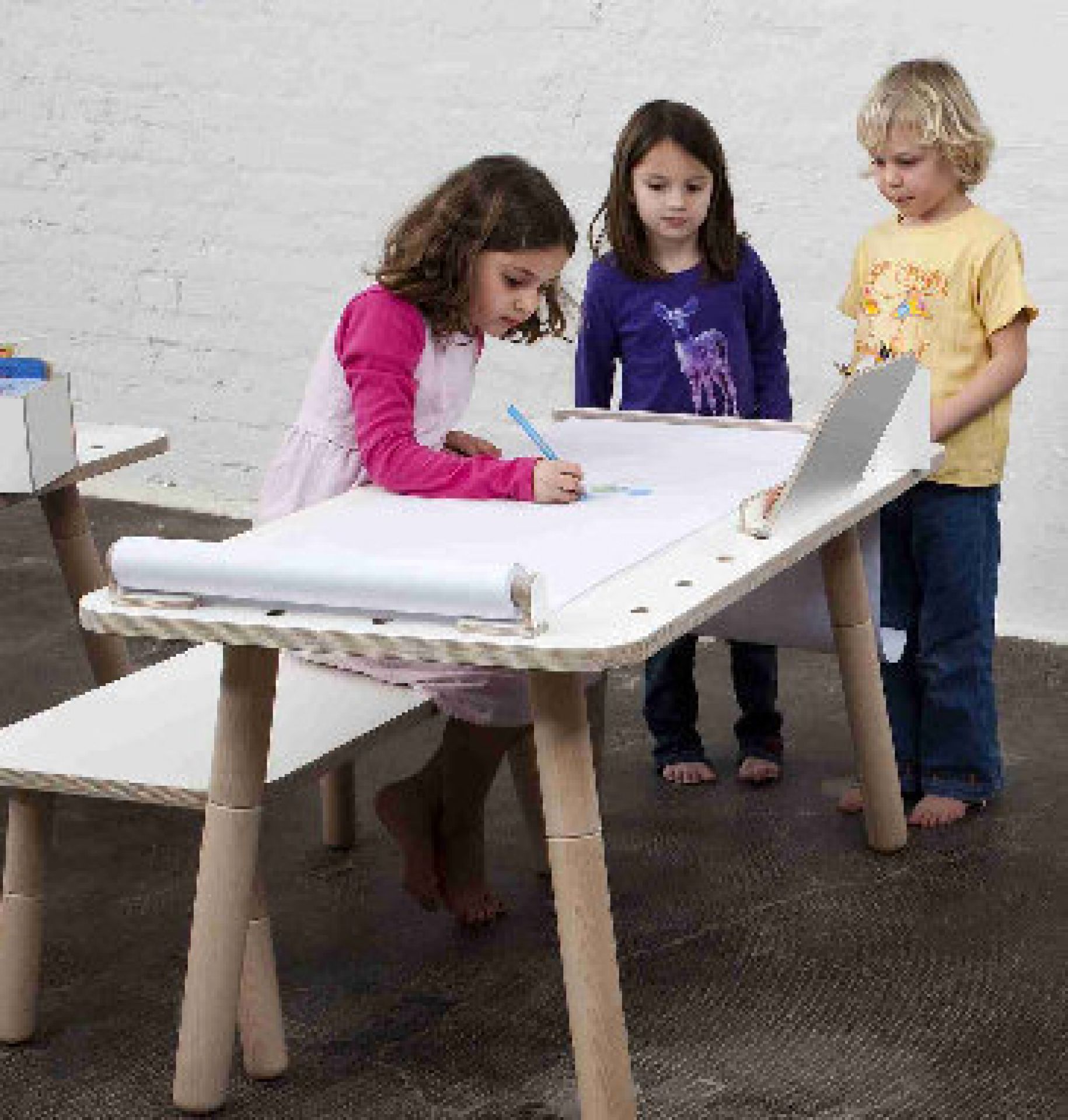 Kinder zeichnen am Kindertisch mit Zeichenrollenhalterung. Kreatives Spielen mit Papierrolle am Maltisch.