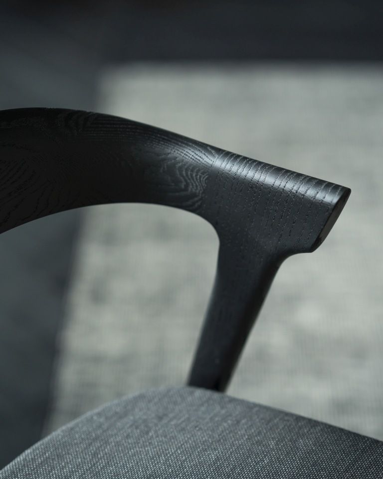 Detailaufnahme des Bok Stuhls von Ethnicraft: Schwarze Eichenholz-Armlehne und grauer Stoffbezug.