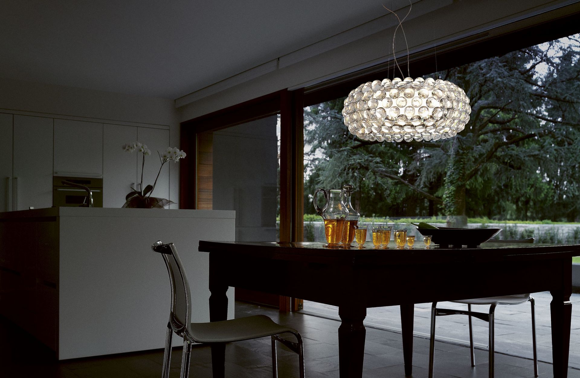 Caboche Media Pendelleuchte von Foscarini in Grau über Esstisch mit Getränken und Blick in den Garten.