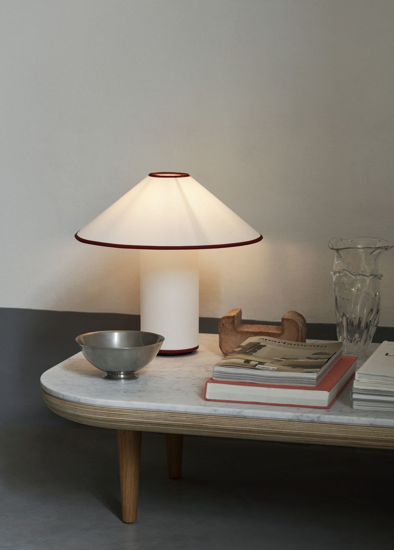 AndTradition Colette ATD6 Tischleuchte auf Marmortisch mit Büchern, Schale und Glasvase.