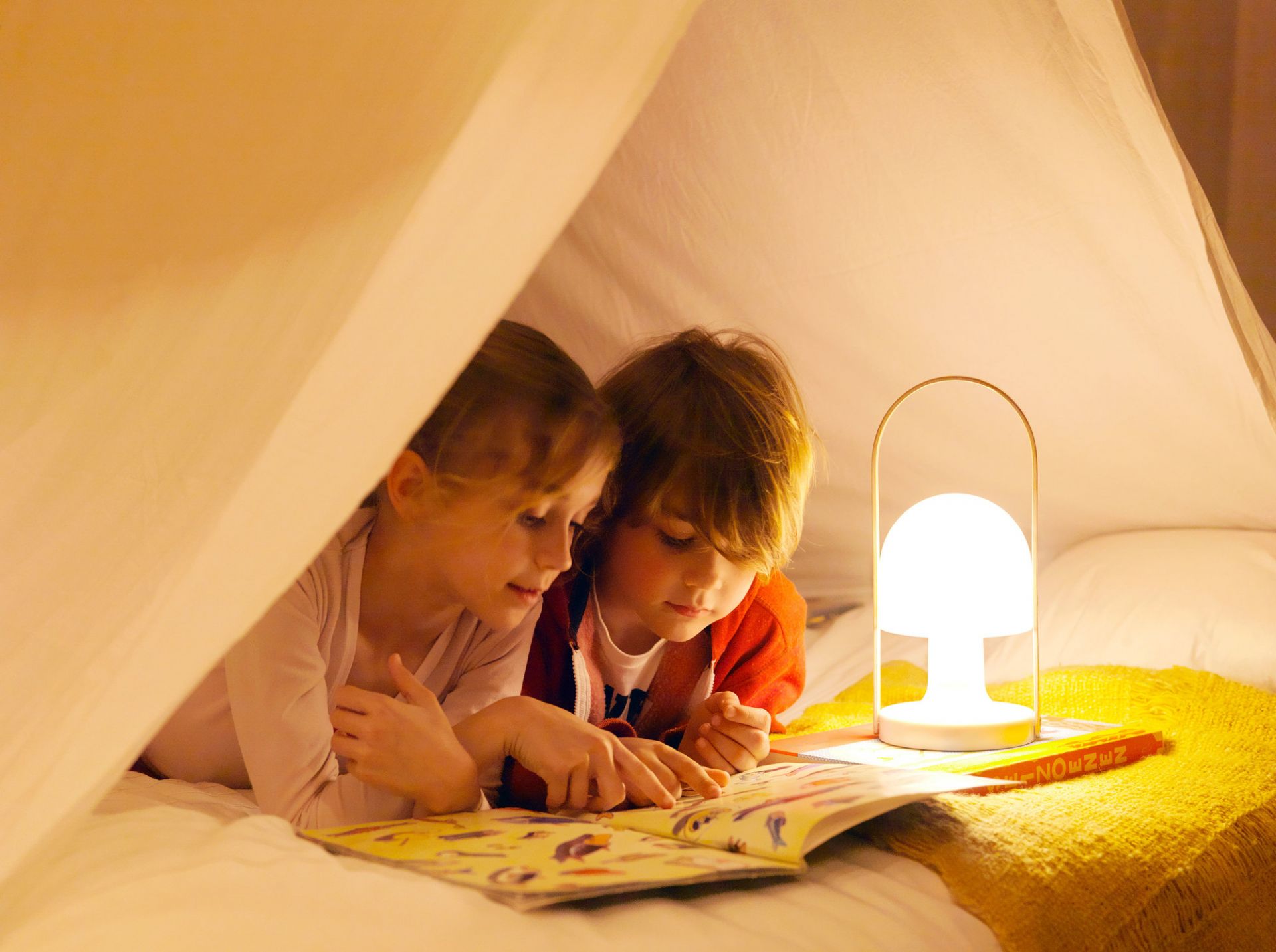 Zwei Kinder lesen im Zelt unter dem Licht der FollowMe LED Akkuleuchte von Marset.