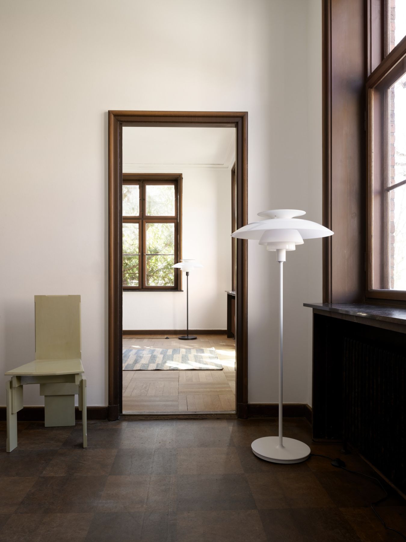 Weiße Stehleuchte im skandinavischen Design mit drei Schirmen und einem Stuhl in einem hellen Raum.