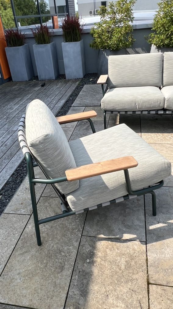 Nahaufnahme der Muuto Settle Lounge Kombination: Outdoor-Sessel mit hellgrauen Polstern und Holzarmlehnen auf Terrasse.