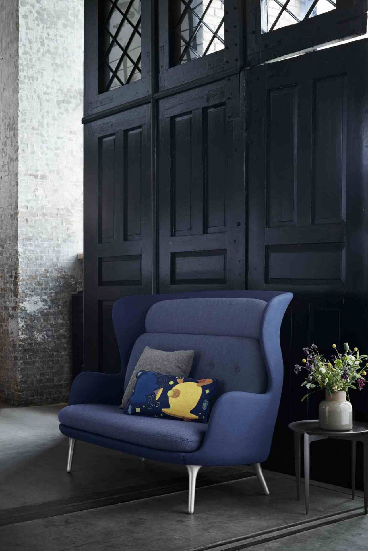 Blaues Ro 2-Sitzer Sofa von Fritz Hansen mit Kissen und Beistelltisch vor dunkler Holzwand.
