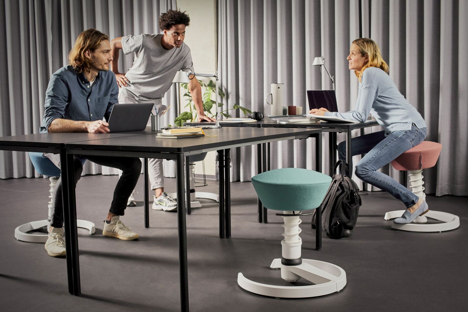 Büroszene mit Personen auf Swopper Hocker von Aeris, ergonomische Sitzmöbel für dynamisches Sitzen.