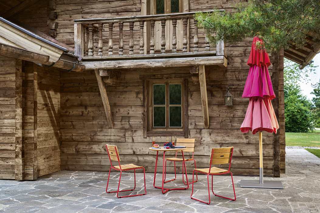 Weishäupl Klassiker Sonnenschirm in Pink-Rot neben Holzhütte mit Gartentisch und Stühlen für entspannte Stunden im Freien.