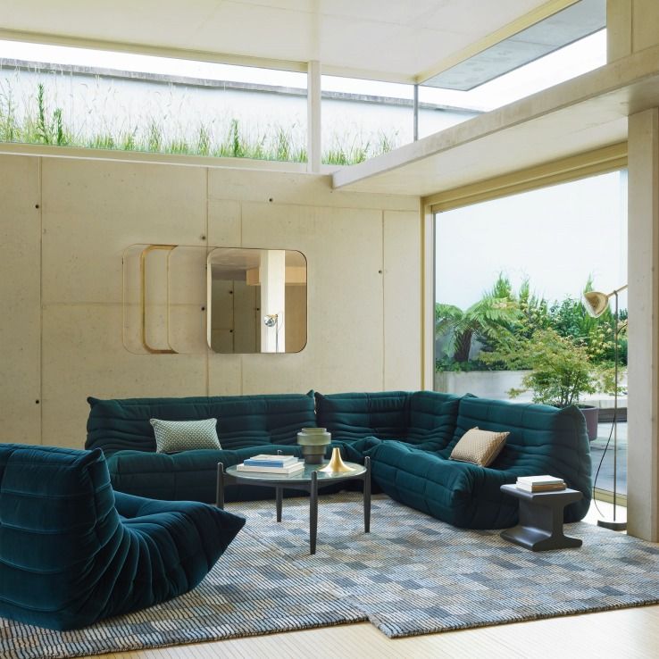 Dunkelblaues Togo Sofa von ligne roset in modernem Wohnzimmer mit großem Fenster und Designermöbeln.
