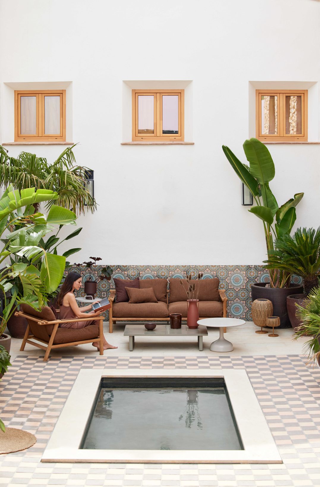Frau liest auf Cane-Line Sticks Outdoor Sofa mit Kissen in mediterranem Gartenambiente.