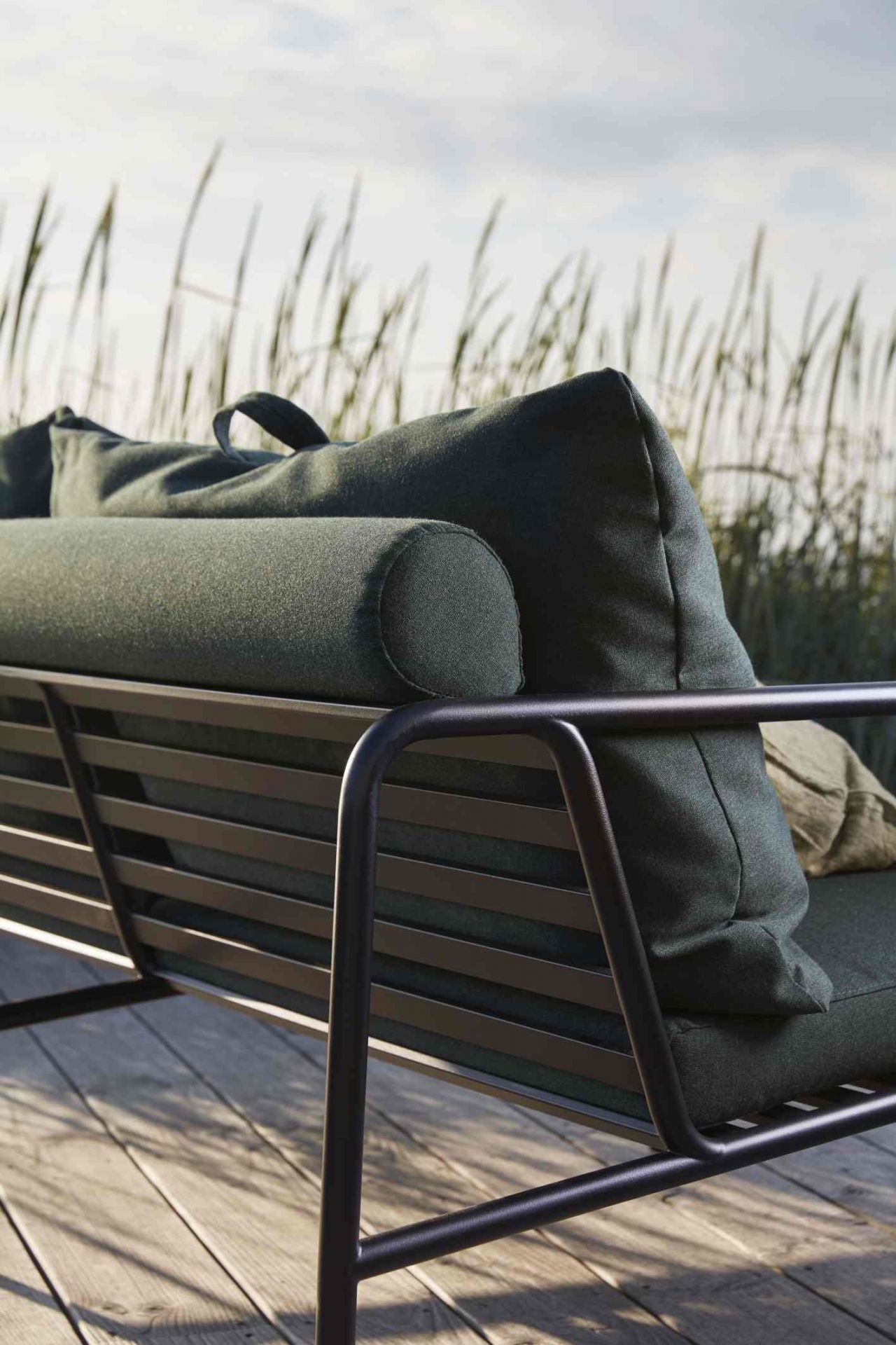 Detailaufnahme des Avon Outdoor Sofas von Houe mit dunkelgrünen Kissen und schwarzem Metallrahmen.