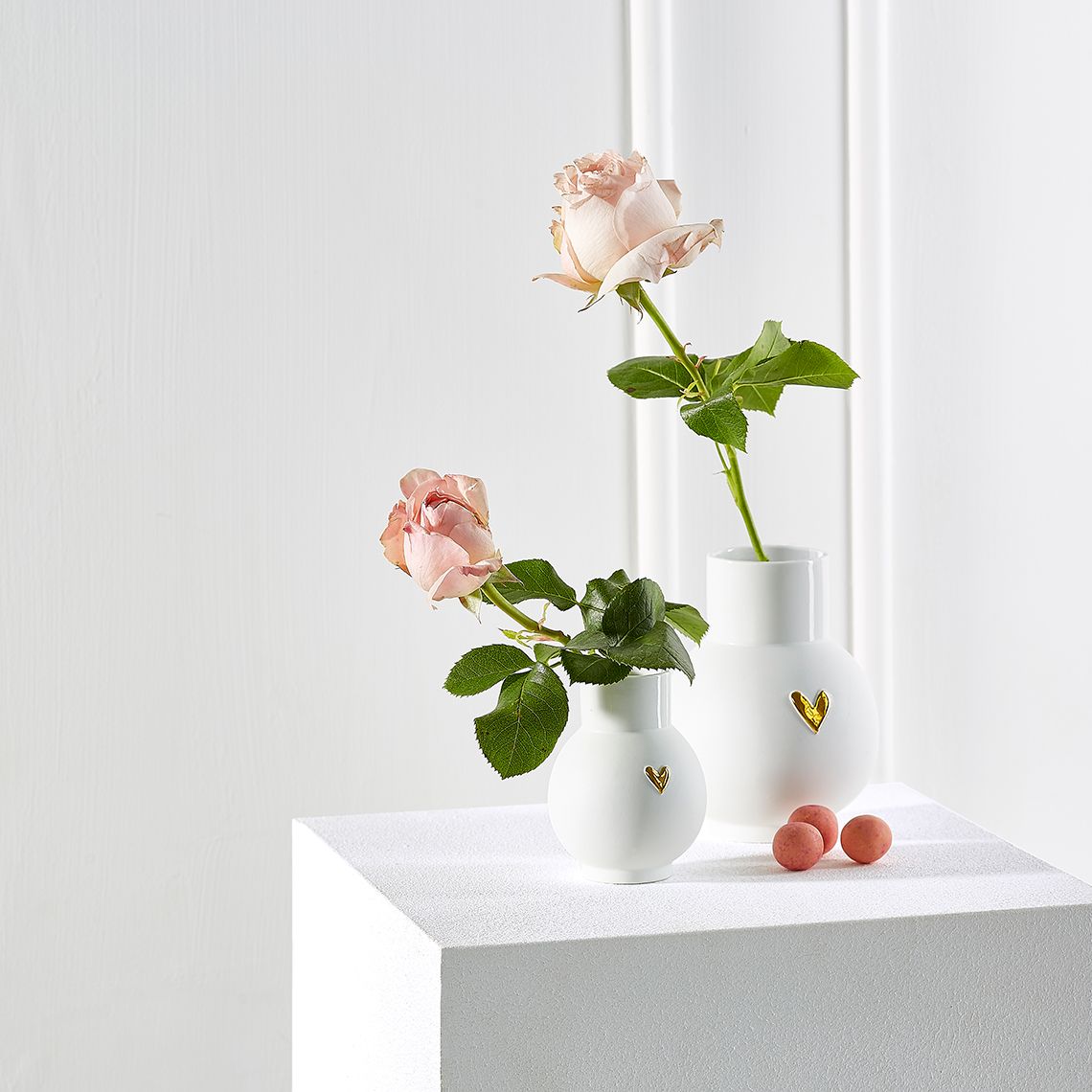 Zwei weiße Kugelvasen mit goldenen Herzen und Rosen, Dekoration für Zuhause.