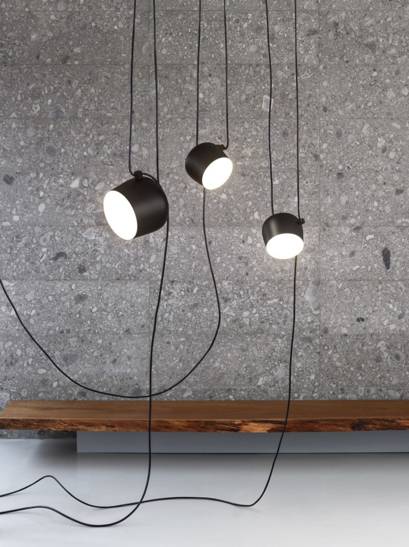 Drei schwarze Aim Pendelleuchten von Flos hängen vor einer grauen Wand. Moderne Innenbeleuchtung.