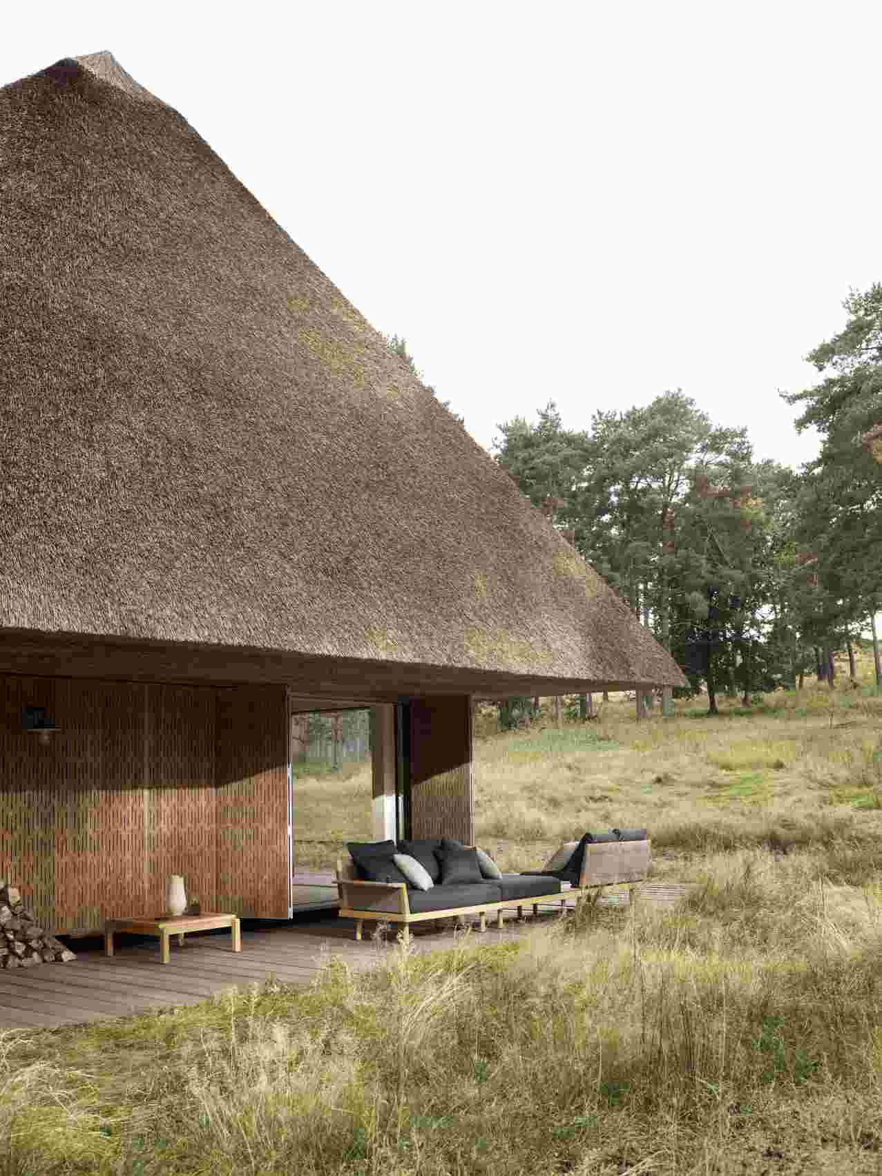 E023 Embrace Lounge Tisch Outdoor von Carl Hansen & Søn vor einem reetgedeckten Haus.