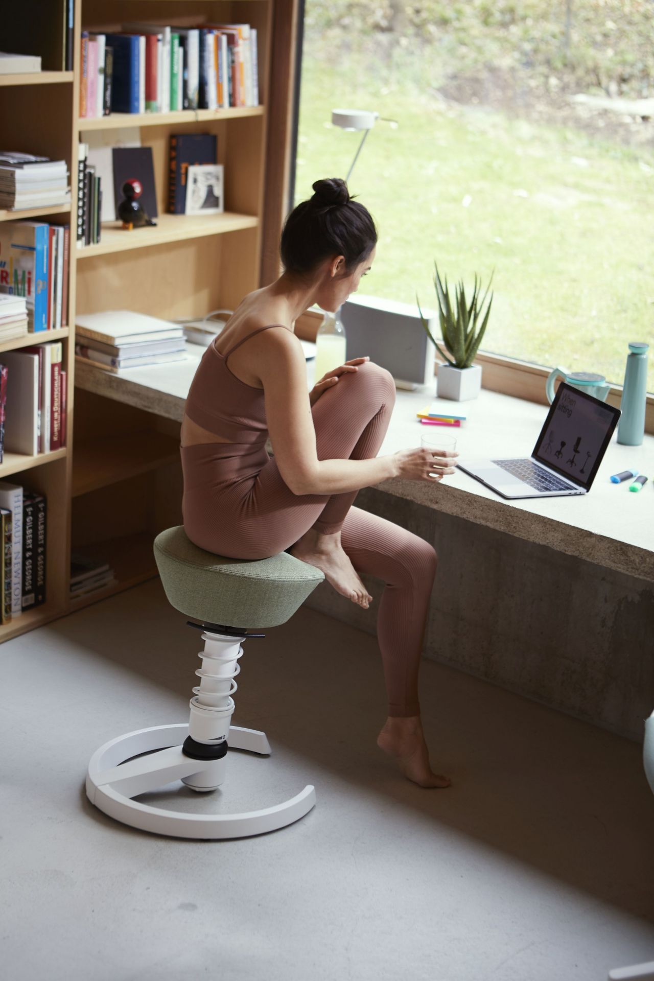 Frau sitzt auf grünem Swopper Bürostuhl vor Laptop am Schreibtisch, ergonomisches Sitzen für Homeoffice.