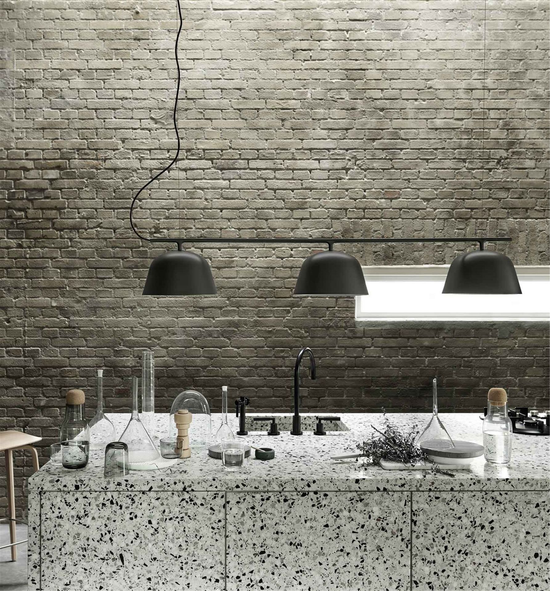 Schwarze Ambit Rail Lamp Pendelleuchte von Muuto über einer Kücheninsel mit Terrazzo-Arbeitsplatte vor einer Backsteinwand.
