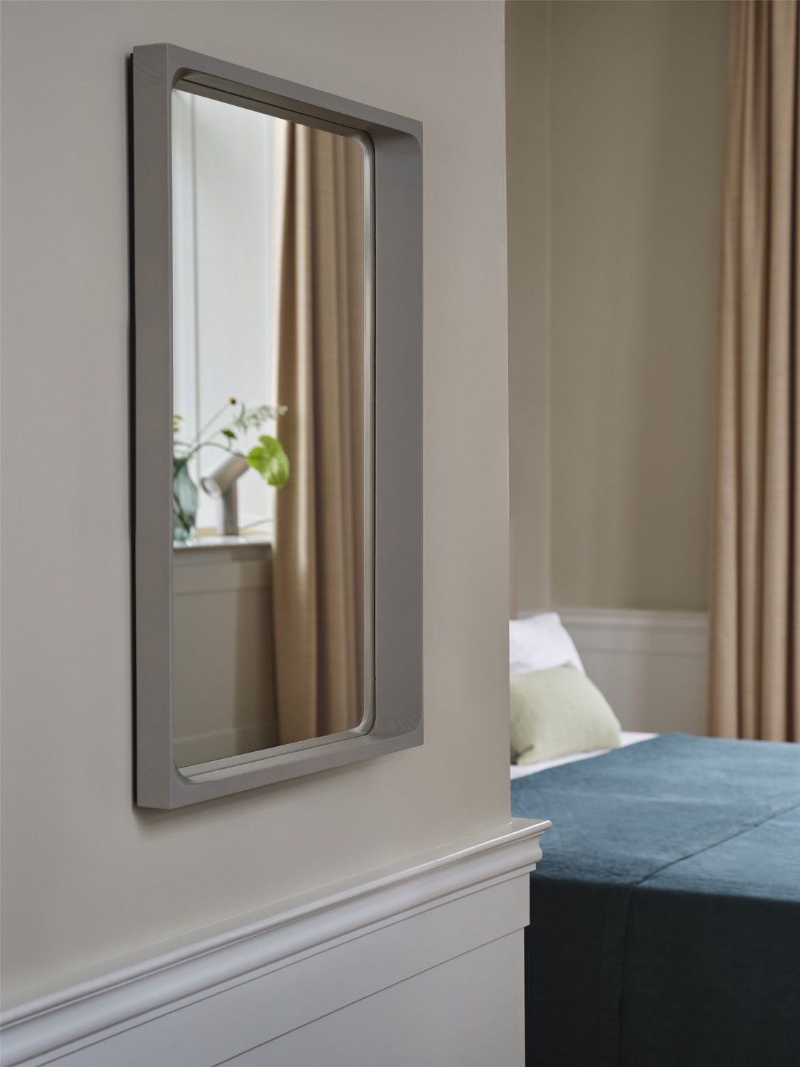 Grauer Arced Mirror Spiegel von Muuto an einer Wand im Schlafzimmer, reflektiert Blumen und Tageslicht.