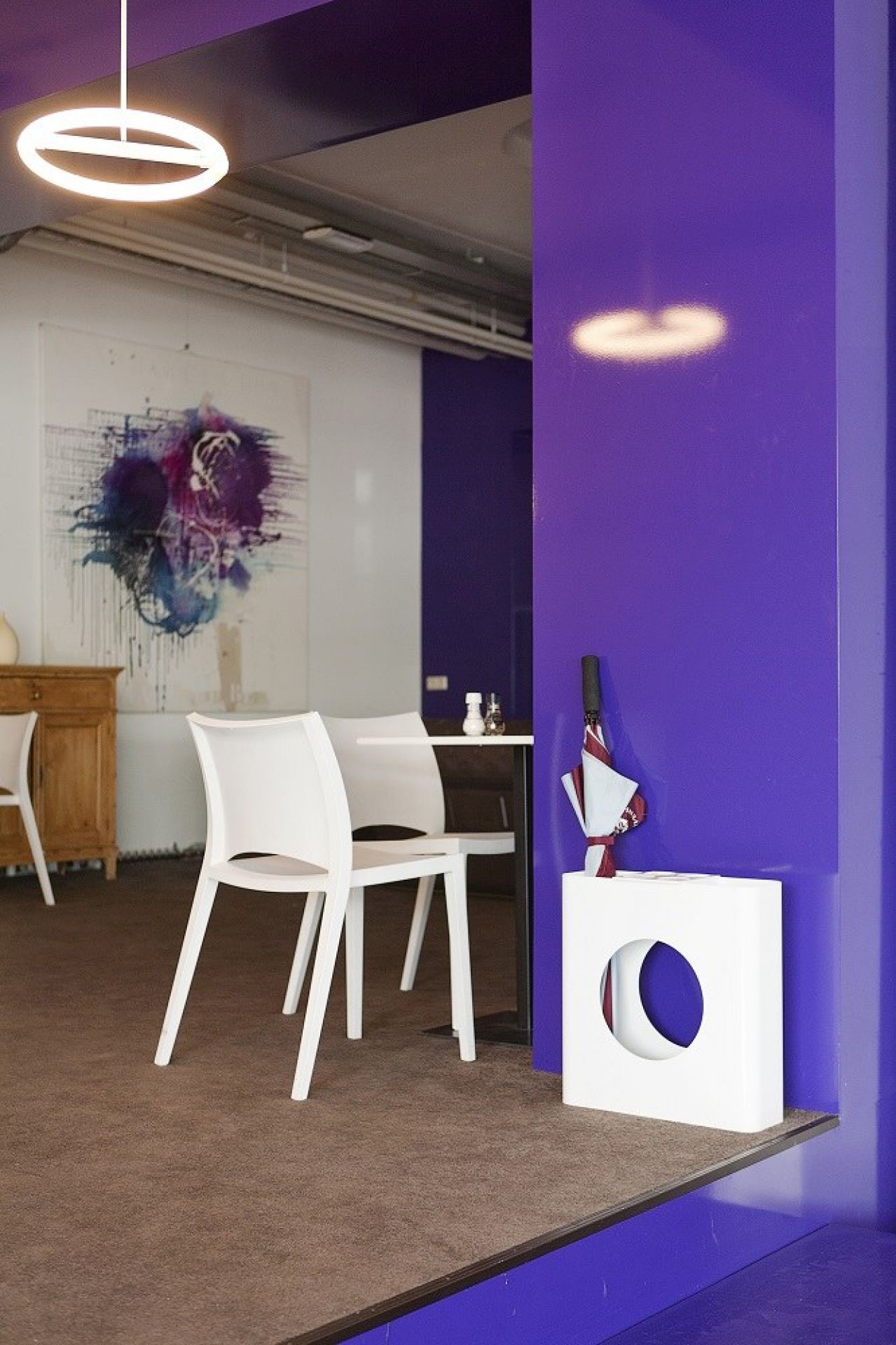 Helle, moderne Café-Szene mit weißen Stühlen, Kunstwerk und lila Akzentwand, inklusive weißem Schirmständer mit Regenschirm.