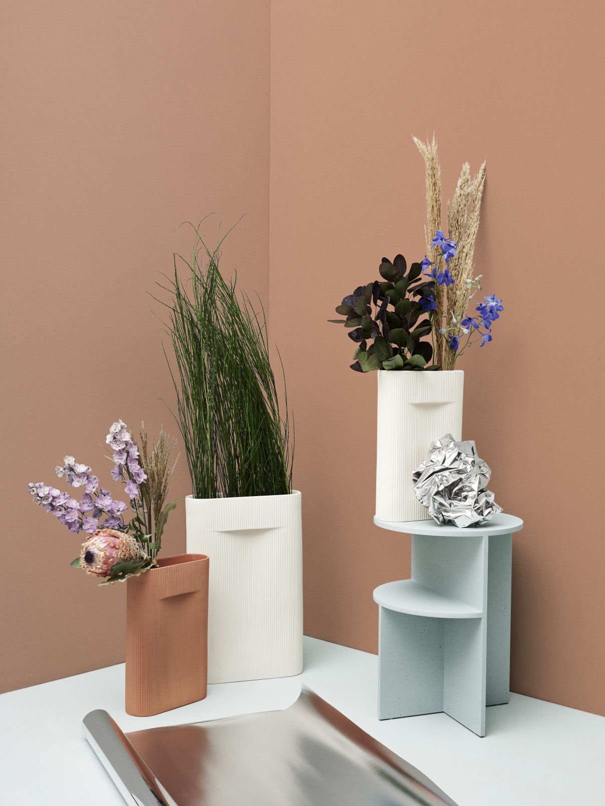 Stillleben mit Muuto Ridge Vase in Weiß und Terrakotta, gefüllt mit Blumen und Gräsern.