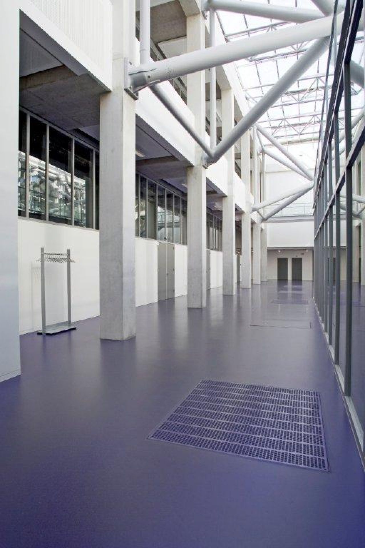 Helle Industriehalle mit lila Epoxidharzboden, Metallgitter, Fensterfronten und Stahlträger-Deckenkonstruktion für moderne Architektur und Design.