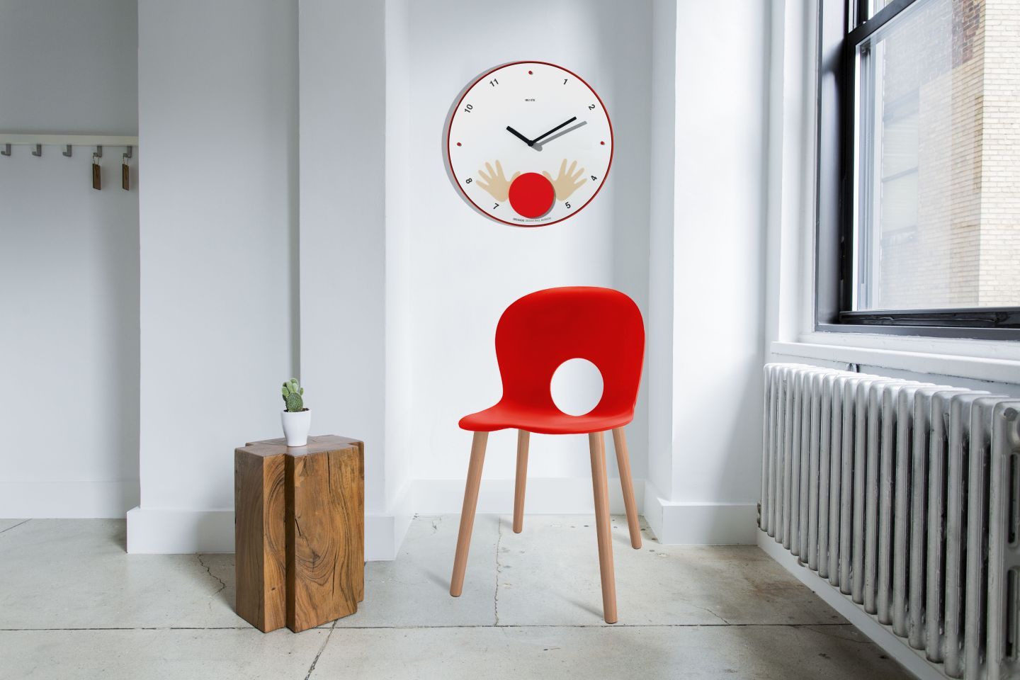 Appuntamento Wanduhr von Rexite, rote Designeruhr mit Händen als Motiv, im modernen Wohnraum mit Stuhl.