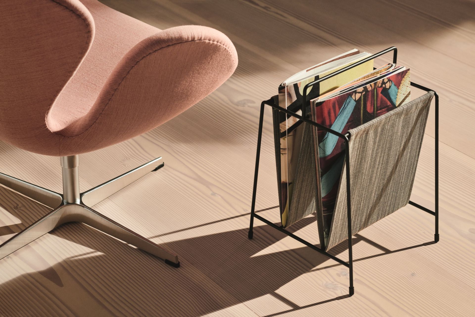 Nahaufnahme des Fritz Hansen Schwan Sessels in Rosa mit einem schwarzen Zeitschriftenständer auf einem Holzboden.