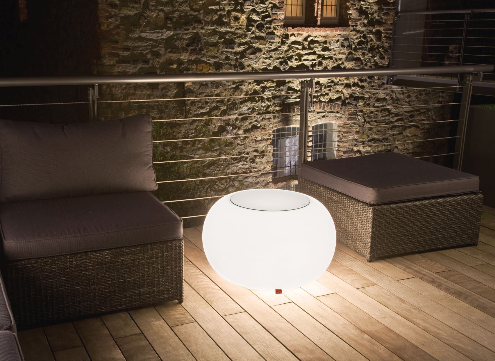 Moderne Outdoor-Lounge mit Kissen, Hocker und runder, leuchtender LED-Tischleuchte für Garten oder Terrasse.
