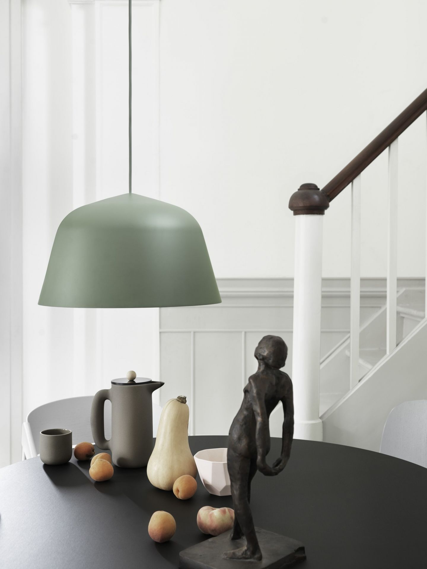 Grüne Muuto Ambit Pendelleuchte über schwarzem Esstisch mit Dekoration, moderne Hängelampe für Esszimmer.