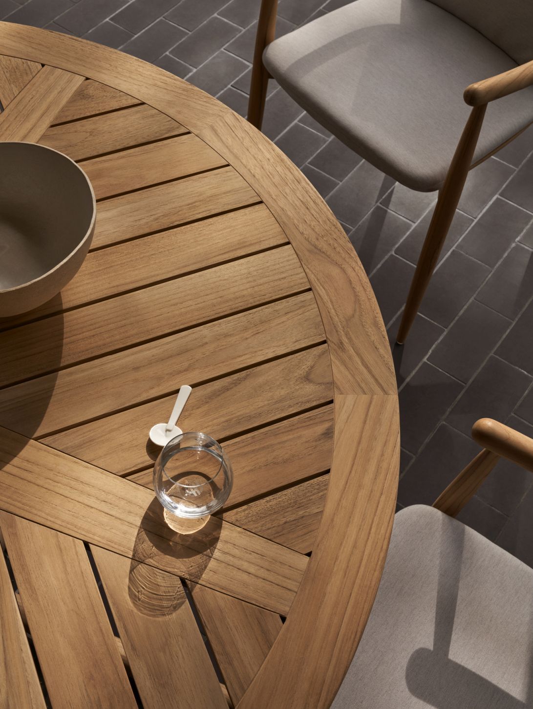 Detailaufnahme des Carl Hansen & Søn E022 Embrace Outdoor Tisches (Ø80cm) aus Teakholz mit Stühlen.