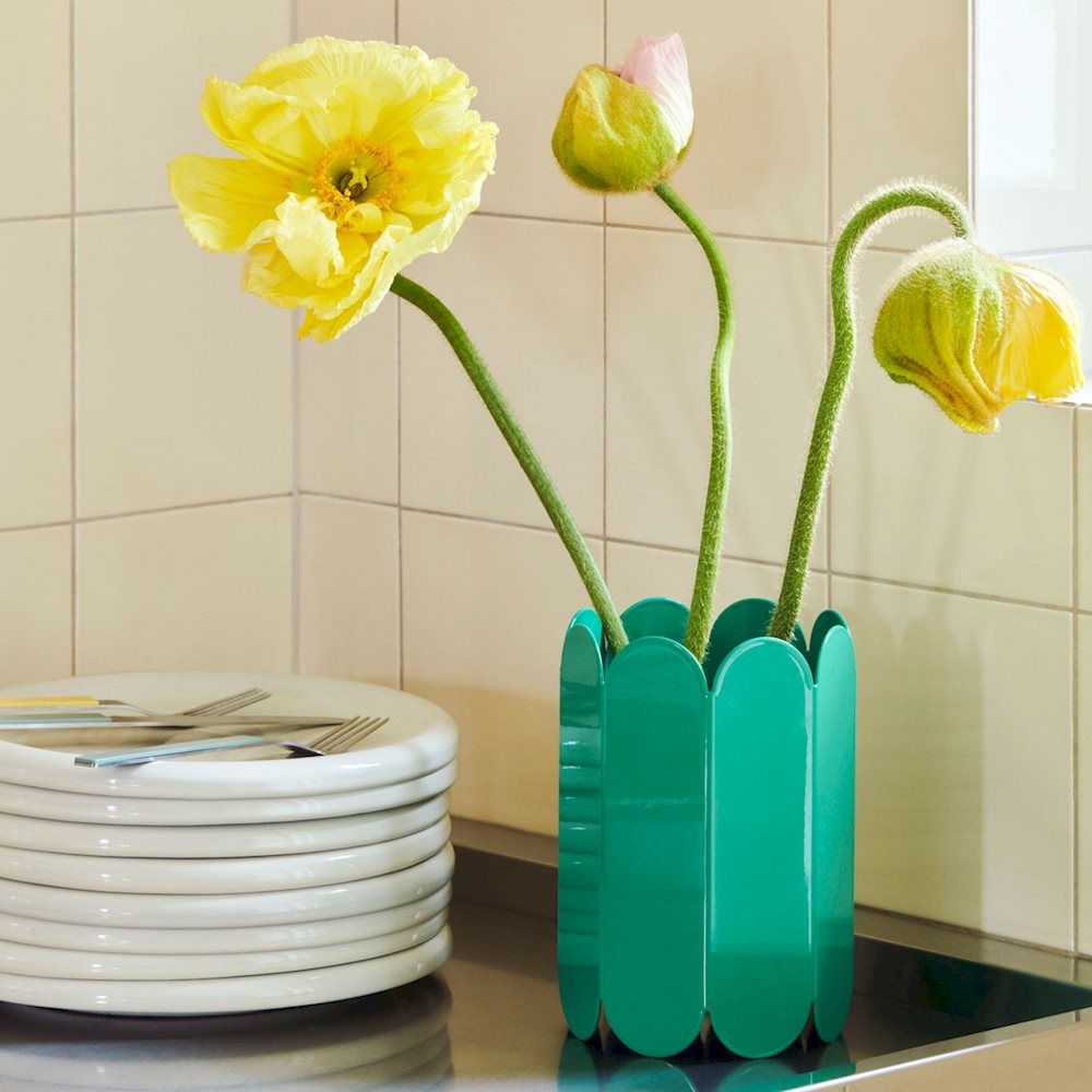 Grüne Arcs Vase von Hay mit gelben Mohnblumen auf einer Küchenarbeitsplatte neben einem Tellerstapel.