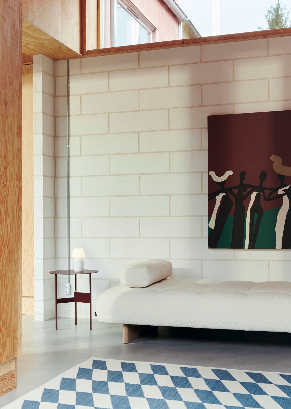 Helles Interieur mit Quilton Daybed Liege von Hay, Nachttisch und blau-weißem Teppich.