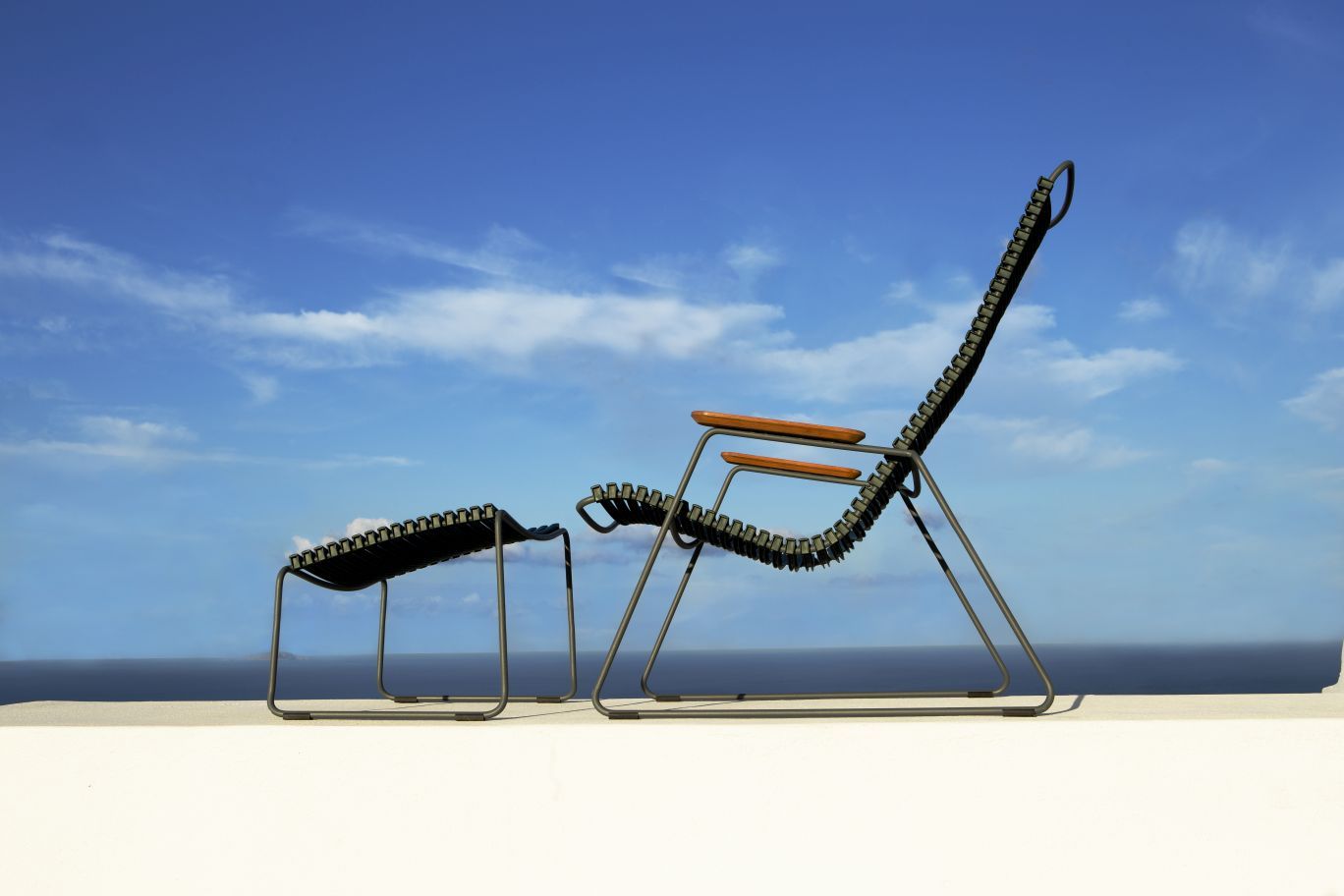 Click Lounge Chair von Houe, Outdoor Sessel mit Fußhocker vor blauem Himmel.