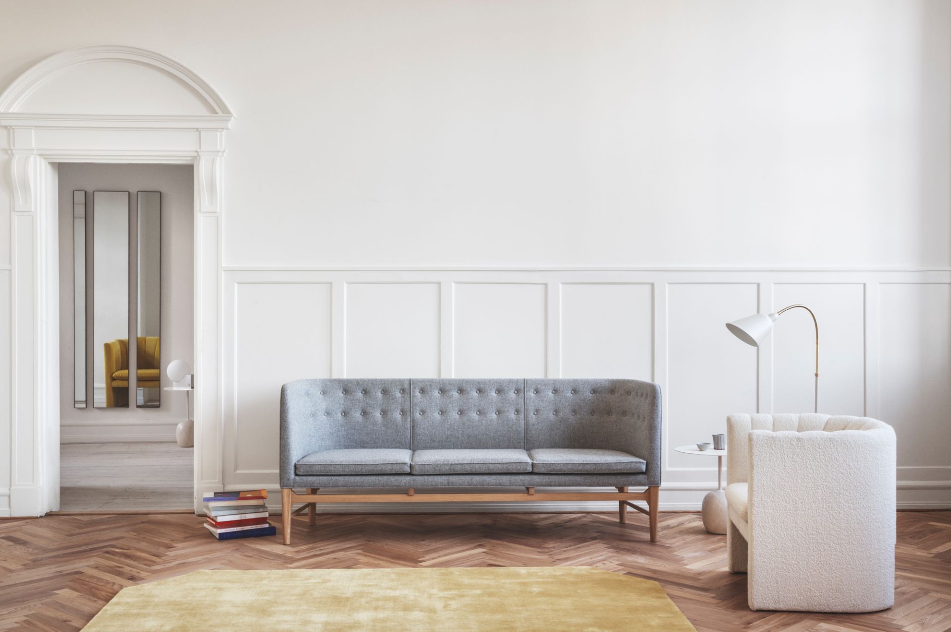 Graues Mayor Sofa von AndTradition im skandinavischen Wohnzimmer mit Sessel, Lampe und Bücherstapel.