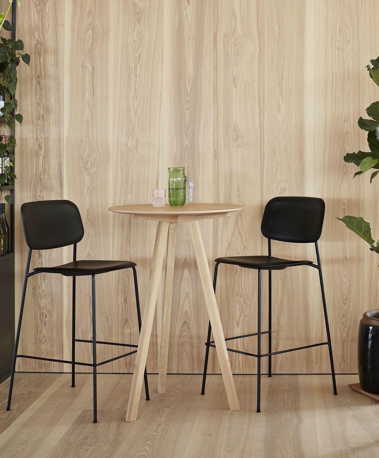 Zwei schwarze Hay Soft Edge Barhocker an einem Holztisch vor einer Holzwand.