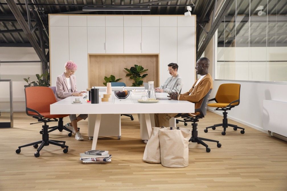 Numo Task Bürodrehstühle von Aeris in Orange und Gelb an einem weißen Konferenztisch mit Personen.
