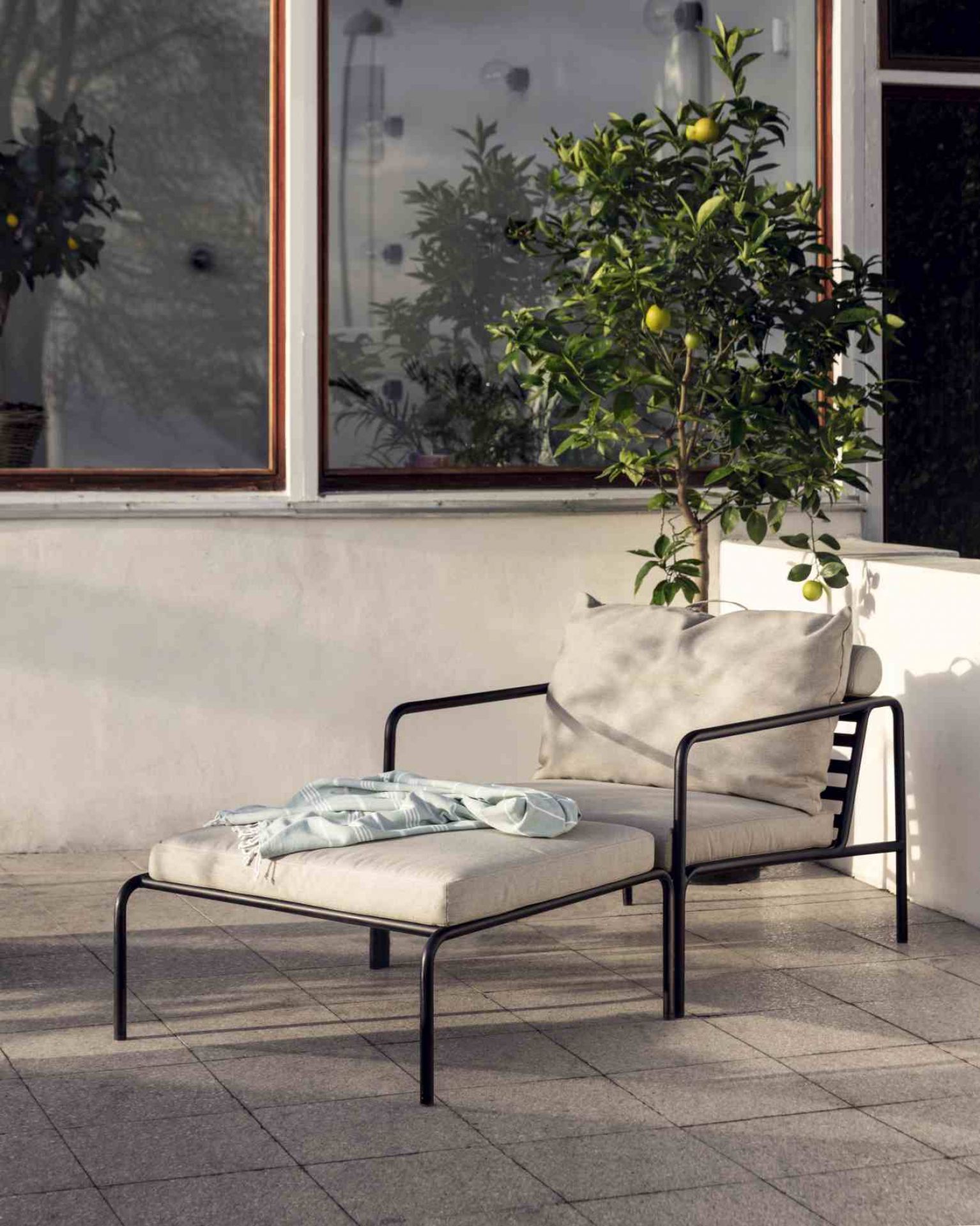 Avon Lounge Chair Outdoor Sessel von Houe mit Fußhocker und hellblauer Decke auf einer Terrasse.
