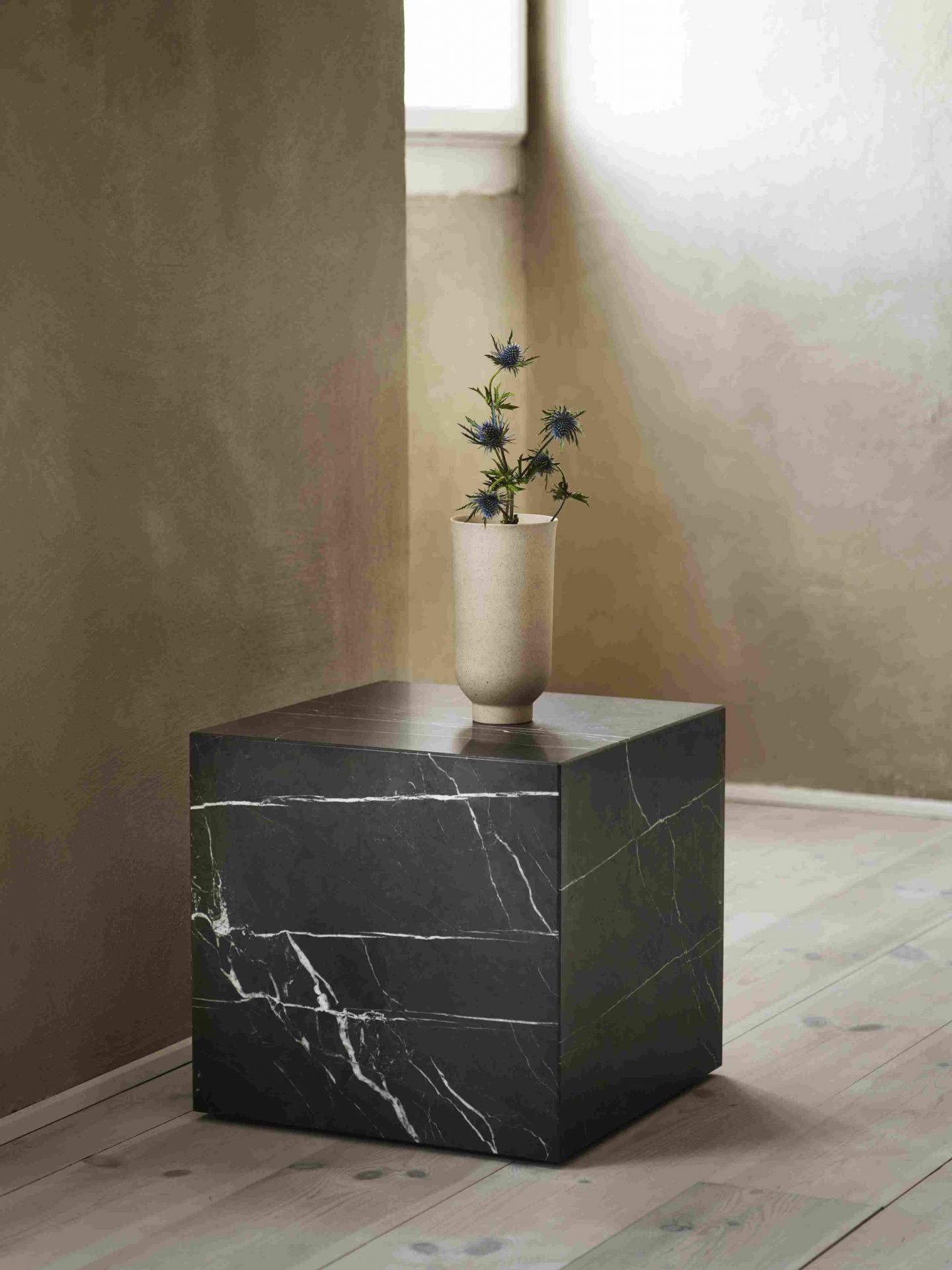 Audo Copenhagen Plinth Tisch aus schwarzem Marmor mit Vase und blauen Disteln.
